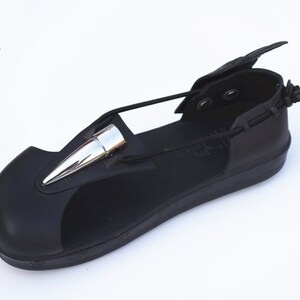 May include: Black leather sandal with a silver spike detail and a strap that wraps around the ankle. The sandal has a black rubber sole and a black leather upper. The sandal is made by Hi-Tek Designs London Alexander.