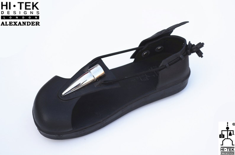 May include: Black leather sandal with a silver spike detail and a strap that wraps around the ankle. The sandal has a black rubber sole and a black leather upper. The sandal is made by Hi-Tek Designs London Alexander.