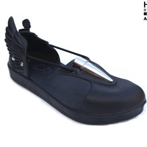 May include: Black leather sandal with a silver bullet detail and a wing design on the back. The sandal has a thick black sole and a black strap across the front. The brand name "HI-TEK DESIGNS LONDON ALEXANDER" is printed on the sandal.