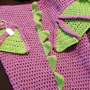 May include: A purple crocheted blanket with green crocheted dinosaur tail and wings.