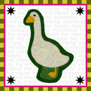 May include: An embroidered patch featuring a white goose with a yellow beak and feet, outlined in dark green. The background is white with repeating light gray text reading singing dog, framed by a yellow and green checkered border with black stars.