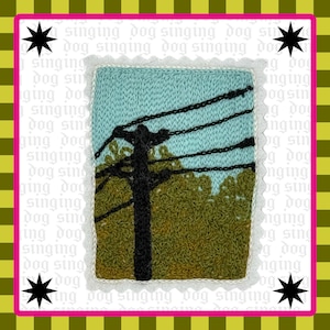 May include: A rectangular textile patch featuring a knitted scene of a black utility pole with dark power lines against a light blue sky and green foliage. The patch has a white scalloped border and is set against a background with green stripes.