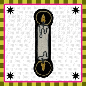 Könnte beinhalten: Gestickter Aufnäher mit einer weißen Kerze mit schwarzen und goldenen Akzenten. Die Kerze hat eine goldene Flamme und ist vor einem schwarzen Hintergrund platziert. Der Aufnäher ist von einem rosa Rand und einem Hintergrund mit dem Text "singing dog singing" umgeben.