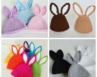 May include: A set of ten crocheted bunny hats in various colors, including pink, blue, purple, orange, green, brown, black, gray, and white. The hats have white bunny ears.