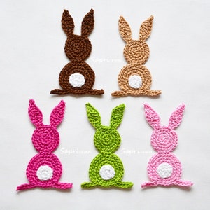 May include: Six crocheted bunny rabbit shapes in different colors. The bunnies are made of yarn and have white felt tails. The colors are brown, beige, pink, green, and two shades of pink.