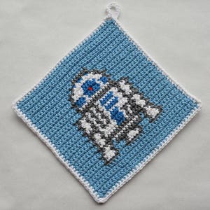 Può includere: Presina quadrata all'uncinetto con un design blu, bianco e grigio di un personaggio robot. La presina ha un bordo bianco e un anello per appenderla. Il design del robot ha un occhio rosso.