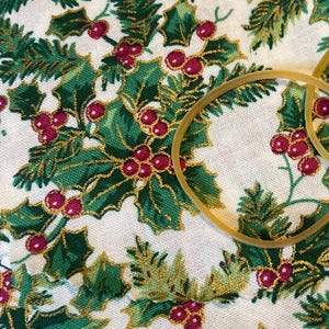 May include: White fabric with a repeating pattern of green holly leaves and red berries with gold accents.