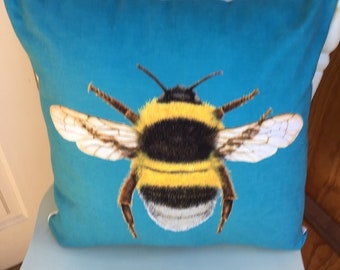 May include: A blue pillow with a bumble bee printed on it. The bee is yellow and black with white fuzzy fur.