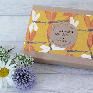 May include: A brown box with a yellow and orange dragonfly pattern. The box has a label that reads "Amber's Country Crafts Lime, Basil & Mandarin Soy Tea Lights Amber's Country Crafts".