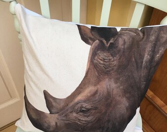 May include: A white throw pillow with a brown rhinoceros face printed on it. The rhinoceros is facing the left side of the pillow and its eye is visible.