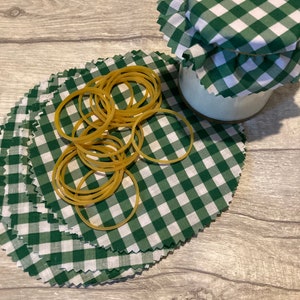 May include: A stack of green and white gingham fabric circles with a pile of rubber bands on top. The fabric circles are used to cover jars.