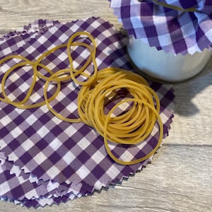 May include: A stack of purple and white gingham fabric squares with a pile of rubber bands on top.