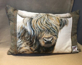 May include: A white pillow with a brown and white Highland cow printed on the front. The pillow has a brown tweed border.