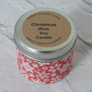 Könnte beinhalten: Eine silberne Dose mit einer Kerze, die mit einem roten und weißen Schneeflockenmuster verziert ist. Das Etikett auf der Kerze lautet "Christmas Wish Soy Candle" und "Amber's Country Crafts".