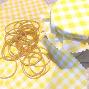 May include: A pile of rubber bands on a yellow and white gingham fabric. The fabric is covering a glass jar.
