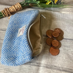 May include: A blue and white herringbone pattern zippered pouch with a beige interior. Several copper coins are scattered nearby. A small label is sewn on the pouch. A bouquet of flowers is in the background.