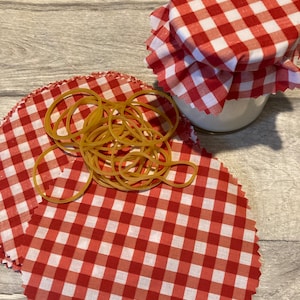 May include: Red and white gingham fabric covers for jars with a rubber band. The fabric covers are reusable and eco-friendly.