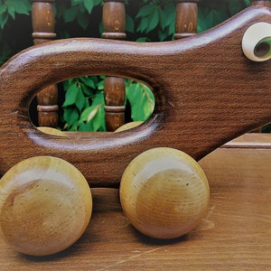 Op de afbeelding: Een houten trekdier in de vorm van een grillig wezen met een donkerbruin lichaam, een grote ovale opening en twee houten wielen. Het speelgoed heeft een lichtgekleurd oog en een kleine glimlach. Het speelgoed staat op een houten oppervlak.