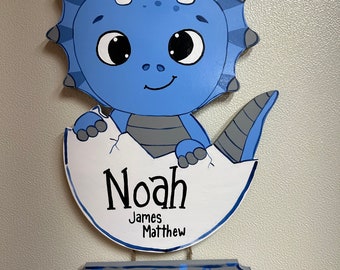 May include: Blue and gray wooden dinosaur baby door hanger with the name Noah James Matthew and a sign that says "Date: Time: RAWr lbs. oz. inches".