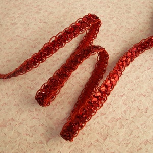 May include: Red sequined trim with a braided design. The trim is made of small, round sequins sewn onto a red fabric base.