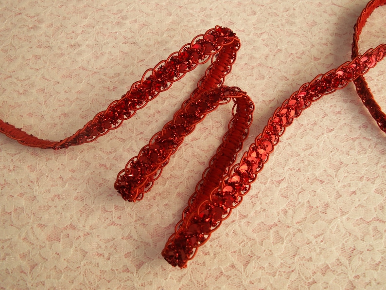 May include: Red sequined trim with a braided design. The trim is made of small, round sequins sewn onto a red fabric base.