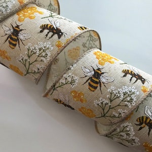 May include: A beige ribbon with a repeating pattern of bees, honeycombs, and white flowers. The bees are black and yellow.