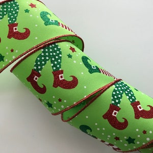 May include: Green ribbon with a red trim featuring a repeating pattern of elf legs and red boots with glitter accents. The background is a light green with white polka dots and green and white stars.
