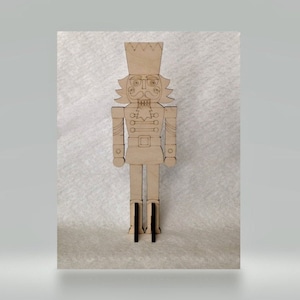 May include: A wooden nutcracker figurine with a brown painted finish. The nutcracker has a tall hat with a crown, a mustache, and a detailed uniform with buttons.
