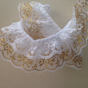 May include: White lace trim with gold glitter accents. The lace is ruffled and has a scalloped edge.