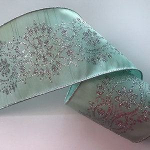 May include: A roll of light teal ribbon with a silver glitter floral design. The ribbon has a silver trim along the edges. This decorative ribbon is suitable for crafts, gift wrapping, and holiday decorations.