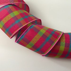 May include: Pink plaid ribbon with a pink edge. The ribbon has a multi-colored plaid pattern with shades of green, blue, orange, and purple.