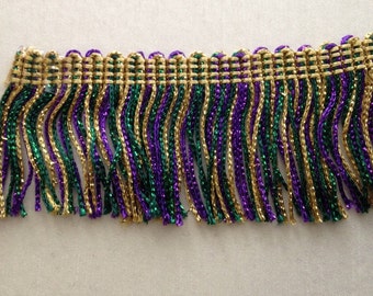 May include: Gold, green, and purple metallic fringe trim. The fringe is made of twisted threads and has a woven top edge.