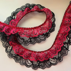 May include: A length of ruffled lace in a vibrant fuchsia pink and black. The lace features a scalloped edge and a delicate floral pattern. The lace is likely used for trimming garments or craft projects.