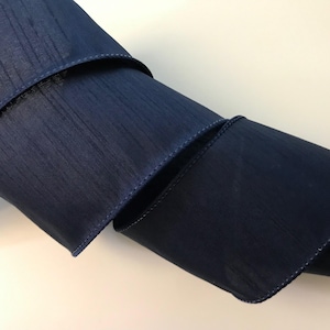 May include: A roll of navy blue wired ribbon with a satin finish. The ribbon is 2.5 inches wide and has a wired edge for easy shaping.