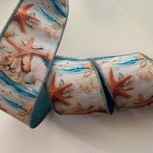 May include: Decorative ribbon featuring a beach scene with orange starfish, seashells, and blue water. The ribbon has a white background with a repeating pattern of marine life. The edges are finished with a blue trim.