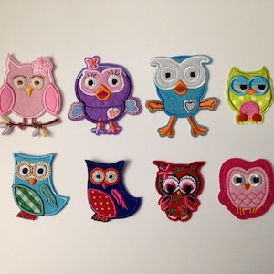 May include: A collection of eight colorful owl-shaped fabric patches. Each patch features a unique design with various colors, including pink, purple, blue, green, and red. The owls have embroidered details and are suitable for crafts or embellishments.