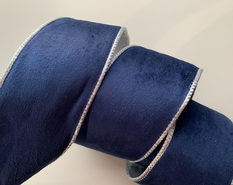 May include: A roll of navy blue velvet ribbon with a silver metallic edge. The ribbon is thick and plush, with a soft texture. The silver edge adds a touch of elegance to the ribbon.
