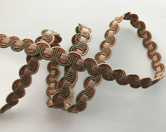May include: A close-up of a decorative trim with a woven texture. The trim is made of three colors: beige, brown, and green. The trim is in a wavy pattern.