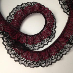 May include: A length of ruffled lace in a burgundy and black color scheme. The lace is intricately designed with a scalloped edge, creating a decorative trim. This lace is suitable for various craft and sewing projects.