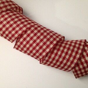 May include: Red and white gingham ribbon with a woven texture. The ribbon is folded and curled.