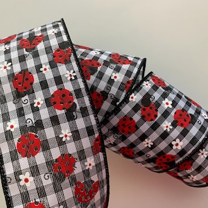 May include: A decorative ribbon featuring a black and white gingham pattern. The ribbon is adorned with red ladybugs and small white flowers. The edges are finished with a black trim. This ribbon is ideal for crafting and gift wrapping.