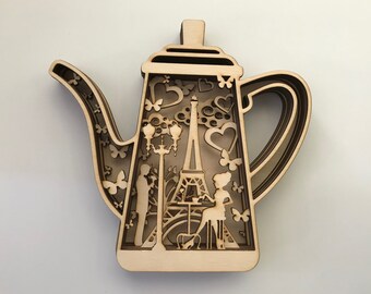 May include: A wooden cutout of a teapot with a Parisian theme. The teapot features an Eiffel Tower, streetlights, hearts, and butterflies. The design is intricate and detailed.