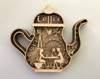 May include: Wooden coffee pot shaped wall decor with a cutout design featuring a couple sitting at a table in front of the Eiffel Tower and a Ferris wheel. The words "Coffee" are written on the top of the pot.