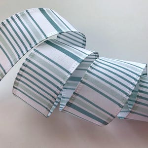 May include: A roll of striped ribbon in white, teal, and light green. The ribbon is curled, showing the pattern of thin, horizontal stripes. The ribbon is likely used for crafts, gift wrapping, or decorative purposes.