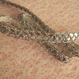 May include: Silver sequined trim with iridescent sequins. The trim is woven and has a raised texture.