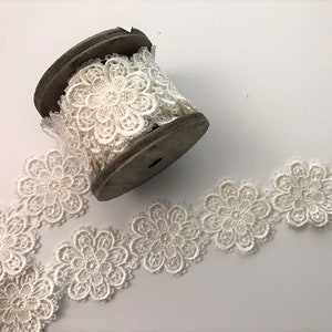 May include: White lace trim with a floral design. The lace is wound around a wooden spool.