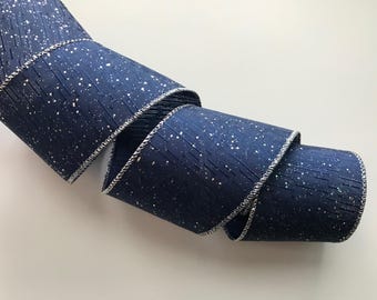 May include: A rolled-up navy blue ribbon with a silver trim. The ribbon has a textured surface with white speckles. The ribbon is a decorative item, likely for crafts or gift wrapping.