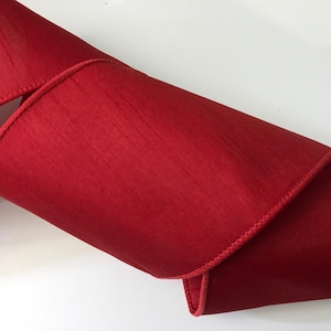 May include: A length of vibrant red ribbon with a subtle sheen. The ribbon is folded and curved, showcasing its texture and the stitched edge. The material appears to be a smooth fabric, perfect for crafting or gift wrapping.