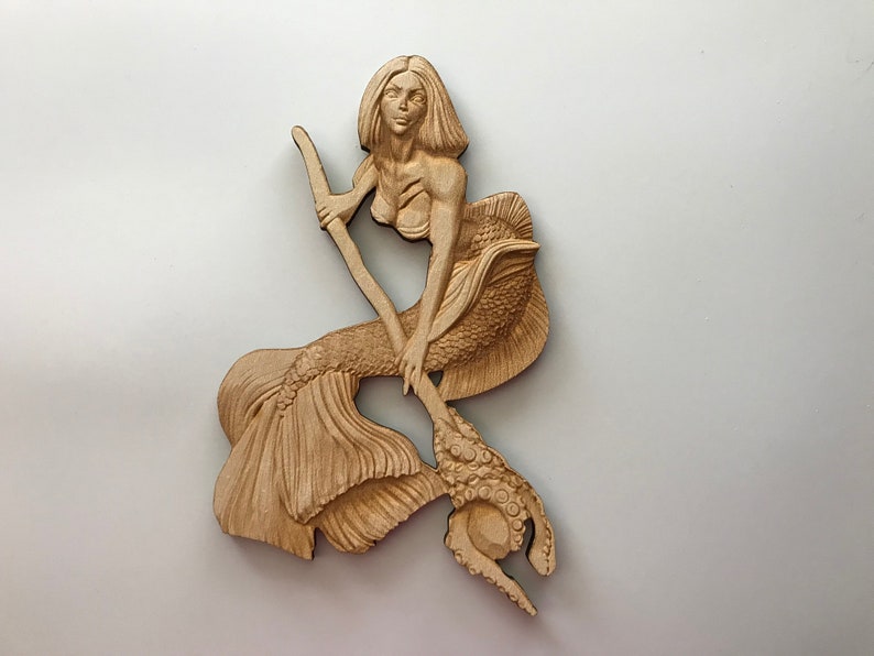 May include: A wooden carving of a mermaid holding a trident with an octopus on the end. The mermaid has long flowing hair and is wearing a seashell bra. The carving is painted in shades of brown.