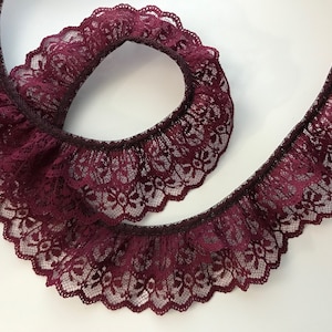 May include: Burgundy lace trim with a scalloped edge and ruffled design. The lace is delicate and has a floral pattern.